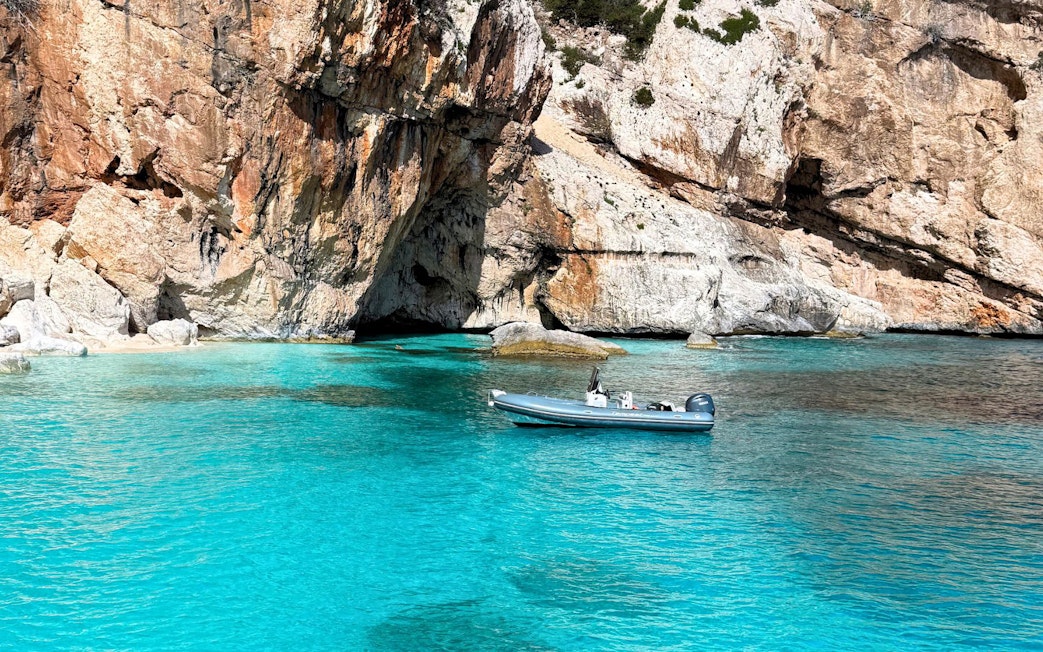 Dinghy in turquoise waters near rocky cliffs, Gulf of Orosei, Cala Gonone.
