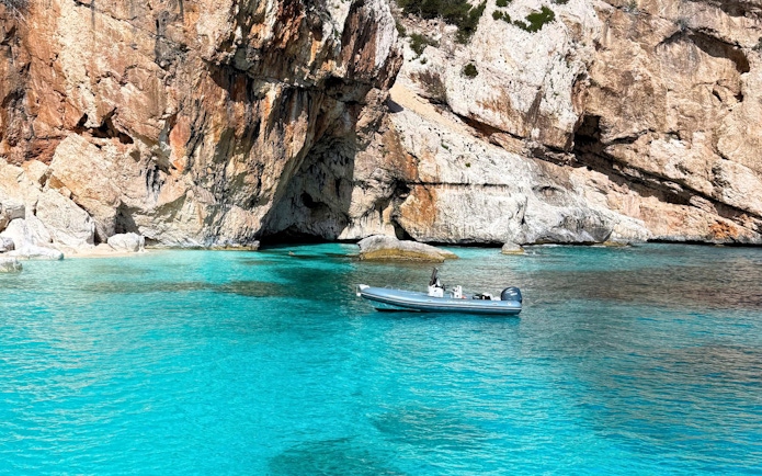 Dinghy in turquoise waters near rocky cliffs, Gulf of Orosei, Cala Gonone.