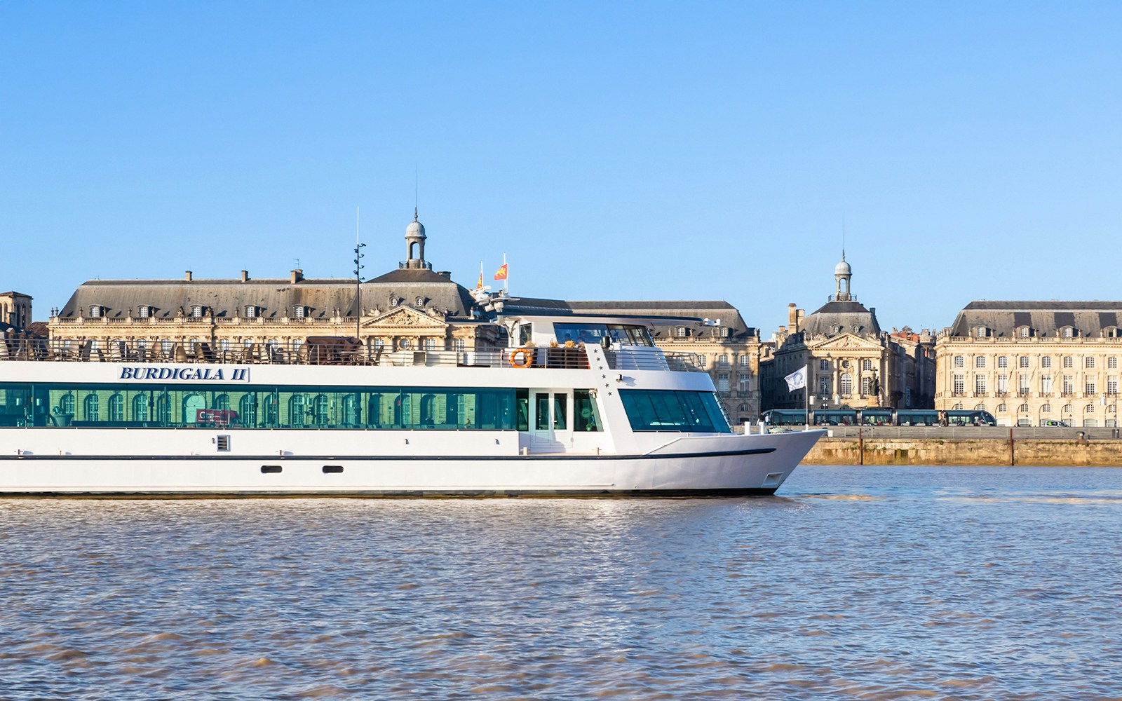 Bordeaux river cruise ship passing by historic buildings on a sunny day.