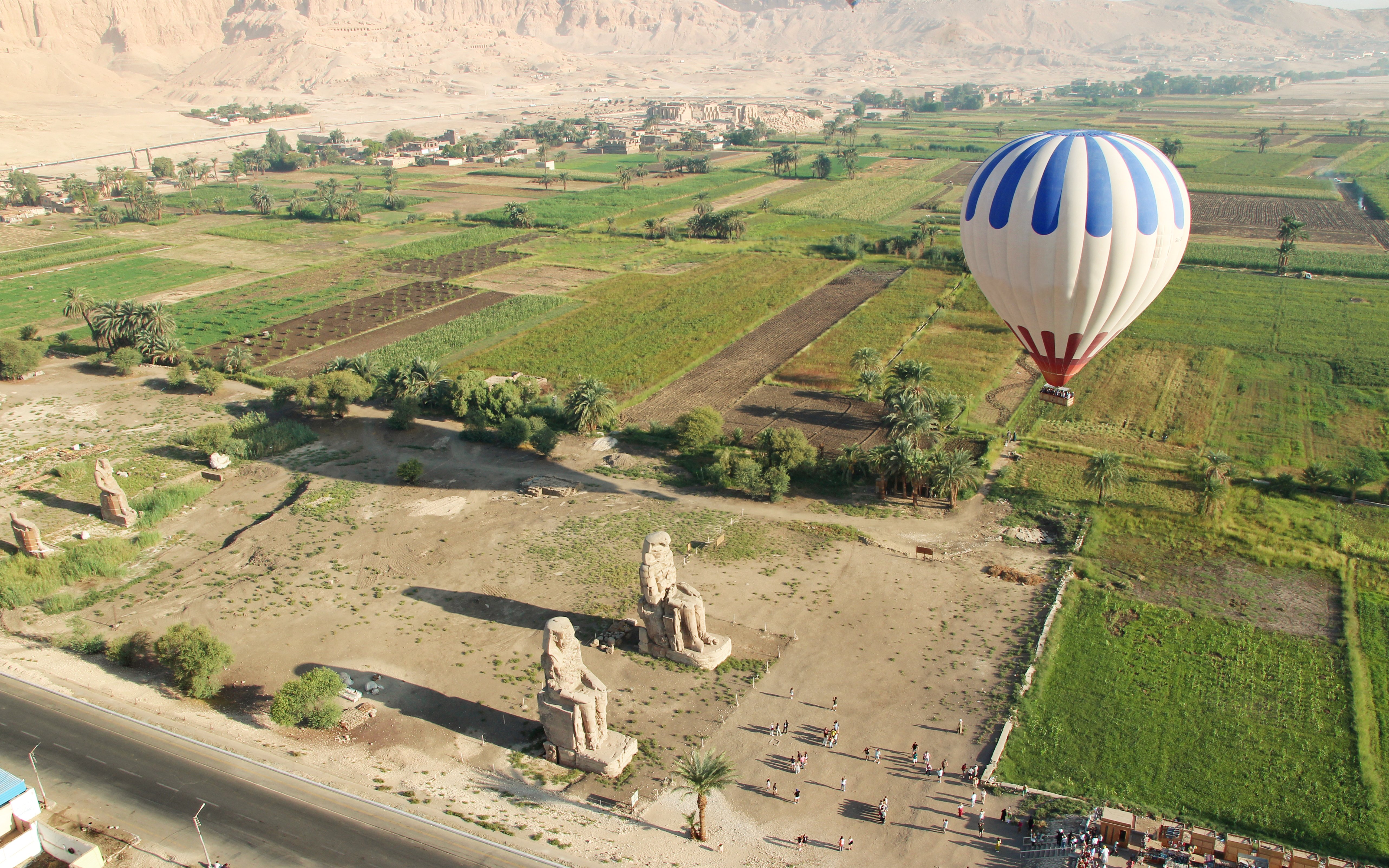 Aerial view of the Colossi of Memnon with a hot air balloon over fields in Luxor, Egypt.