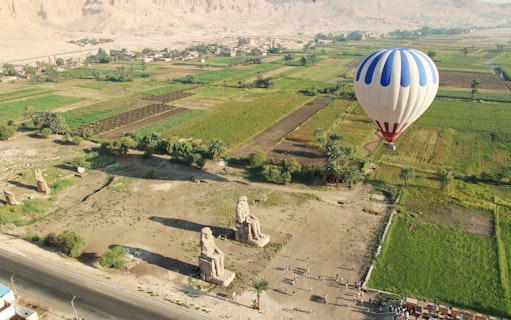 Aerial view of the Colossi of Memnon with a hot air balloon over fields in Luxor, Egypt.