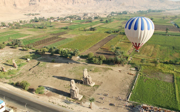 Aerial view of the Colossi of Memnon with a hot air balloon over fields in Luxor, Egypt.
