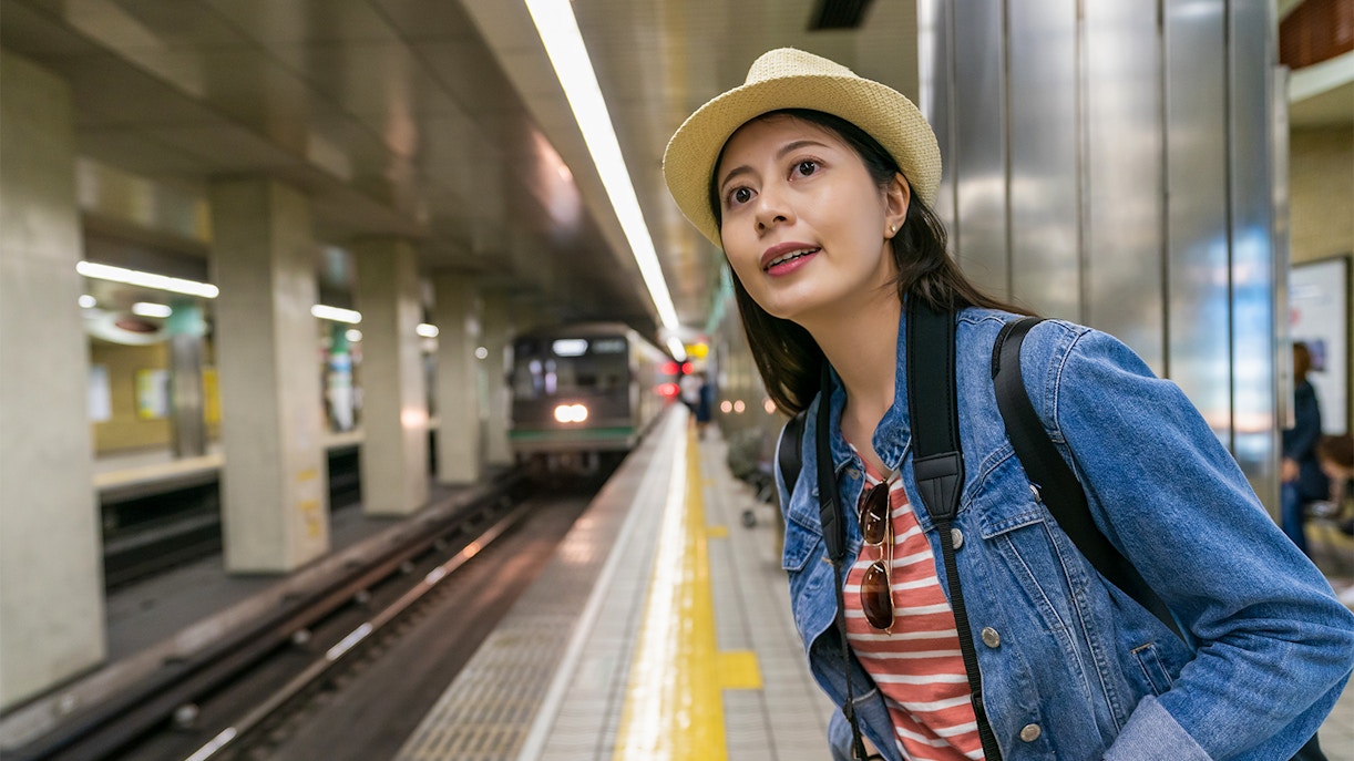 Woman at Osaka Metro station platform with camera, waiting for train using Osaka Metro Tourist Pass.