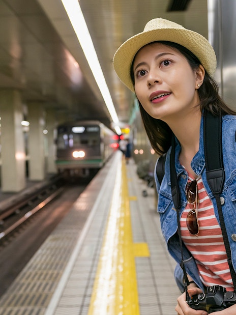Woman at Osaka Metro station platform with camera, waiting for train using Osaka Metro Tourist Pass.