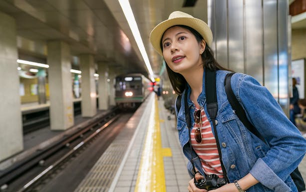 Woman at Osaka Metro station platform with camera, waiting for train using Osaka Metro Tourist Pass.
