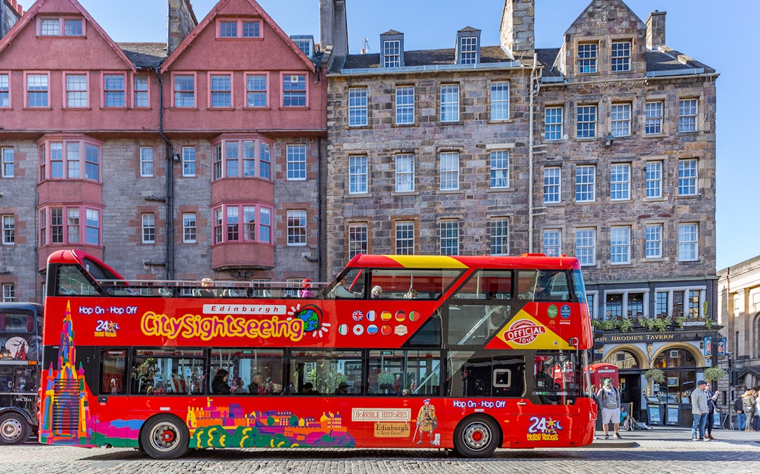 Edinburgh hop-on hop-off bus in front of historic buildings on a city street.