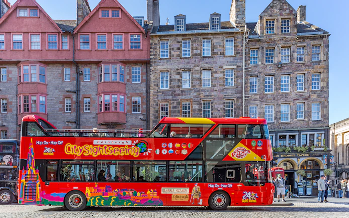 Edinburgh hop-on hop-off bus in front of historic buildings on a city street.