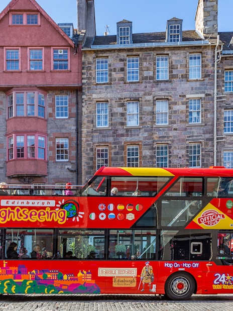 Edinburgh hop-on hop-off bus in front of historic buildings on a city street.