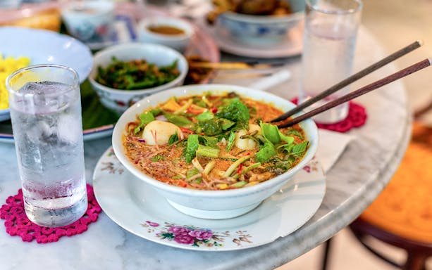 Bowl of noodle soup with herbs and vegetables on a table during a George Town food tour.