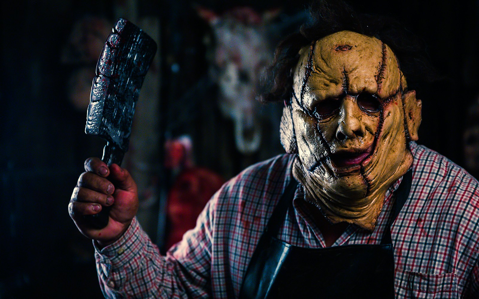 Man in a stitched mask holding a cleaver, wearing a plaid shirt and apron, Halloween costume.