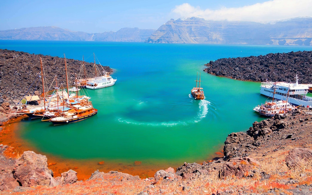 Boats anchored near volcanic island during Santorini Volcano Boat Tour.