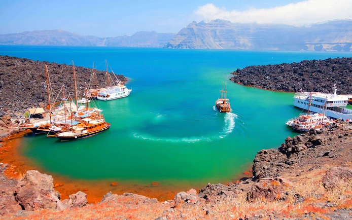 Boats anchored near volcanic island during Santorini Volcano Boat Tour.