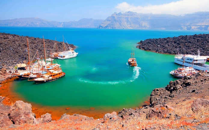 Boats anchored near volcanic island during Santorini Volcano Boat Tour.