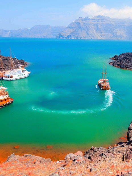 Boats anchored near volcanic island during Santorini Volcano Boat Tour.