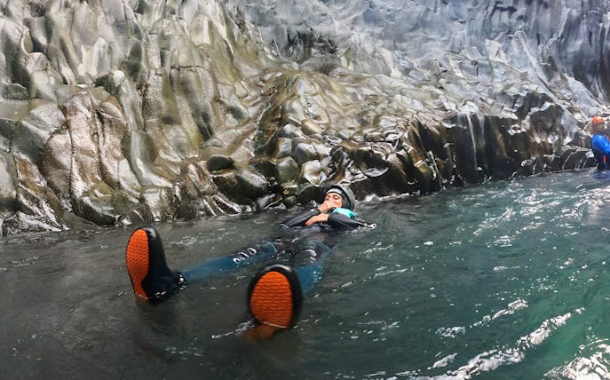 Person body rafting in Gole Alcantara, Sicily, surrounded by rocky canyon walls.