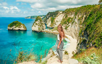 Woman overlooking cliffs and ocean on Nusa Penida Island tour, Indonesia.