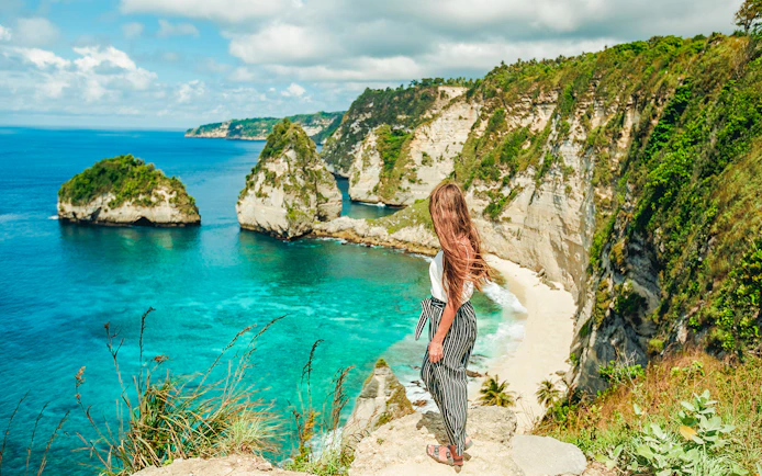 Woman overlooking cliffs and ocean on Nusa Penida Island tour, Indonesia.