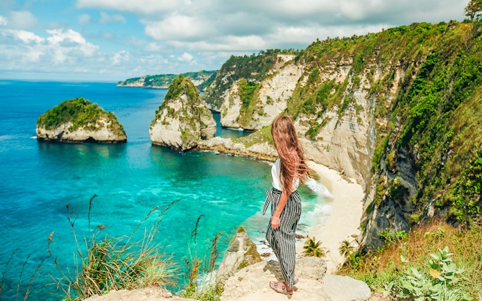 Woman overlooking cliffs and ocean on Nusa Penida Island tour, Indonesia.