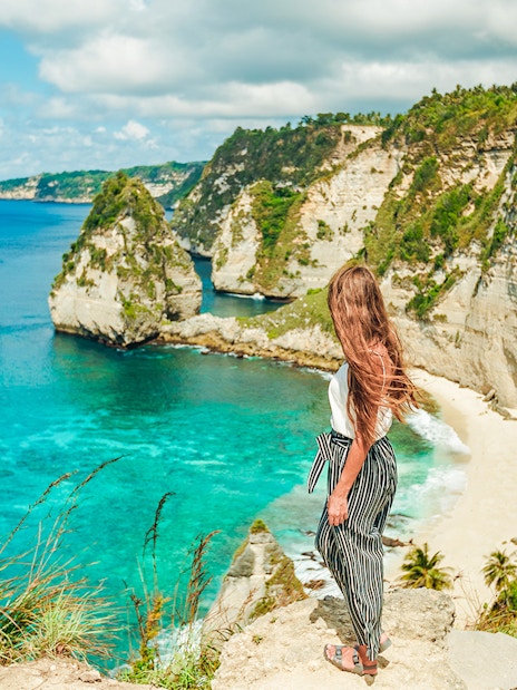 Woman overlooking cliffs and ocean on Nusa Penida Island tour, Indonesia.