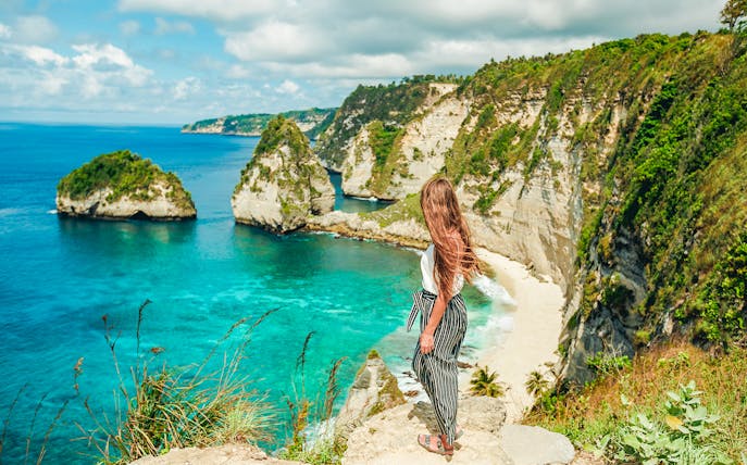 Woman overlooking cliffs and ocean on Nusa Penida Island tour, Indonesia.