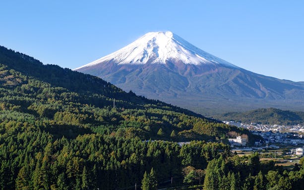 Mt Fuji with snow-capped peak viewed from Hakone, surrounded by lush green forests.
