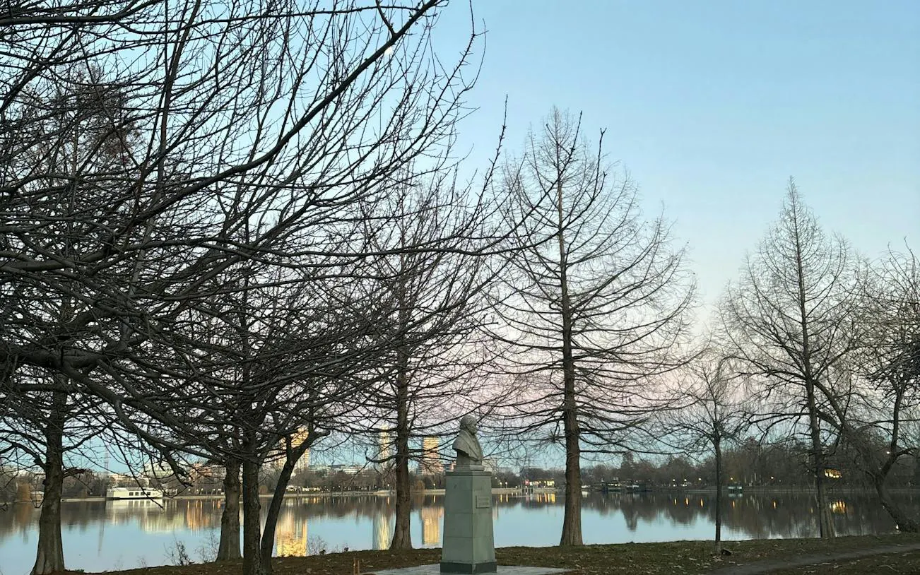 Bust statue near lake with bare trees in Bucharest park.