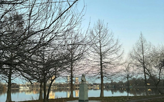 Bust statue near lake with bare trees in Bucharest park.