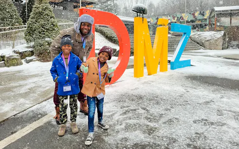 Family posing by colorful DMZ sign in snowy Korean Demilitarized Zone.