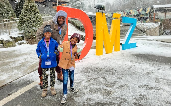 Family posing by colorful DMZ sign in snowy Korean Demilitarized Zone.