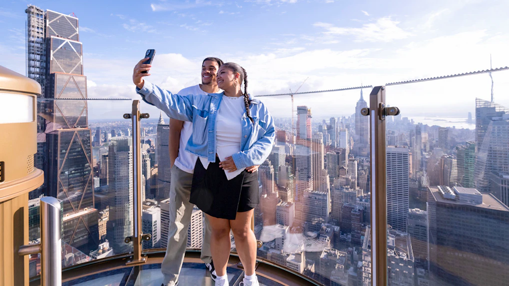 Couple taking a selfie at Top of the Rock with New York City skyline in the background.