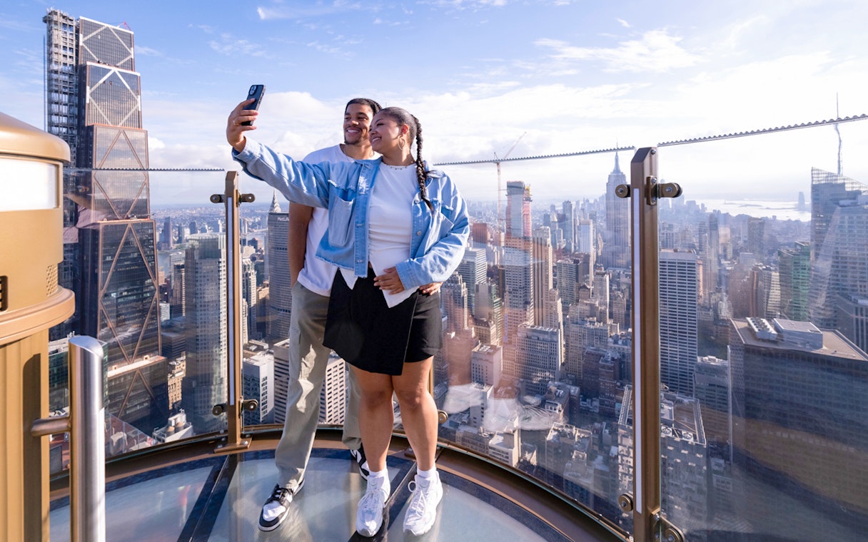 Couple taking a selfie at Top of the Rock with New York City skyline in the background.