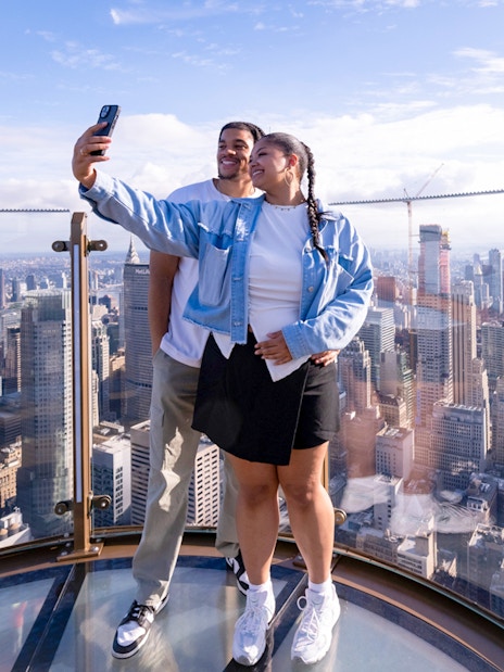 Couple taking a selfie at Top of the Rock with New York City skyline in the background.