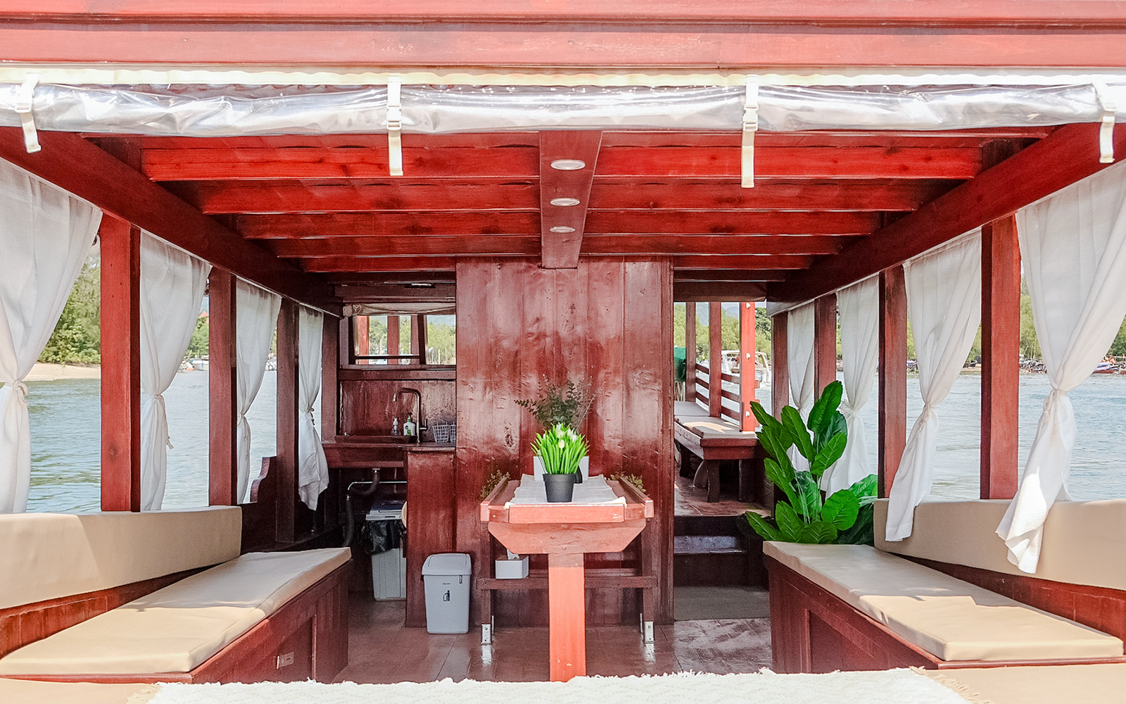 Interiors of a long tail boat in Krabi with wooden seating and potted plants.