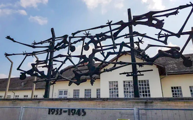 Sculpture at Dachau Concentration Camp memorializing victims, with camp building in background.