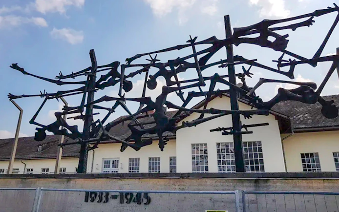 Sculpture at Dachau Concentration Camp memorializing victims, with camp building in background.