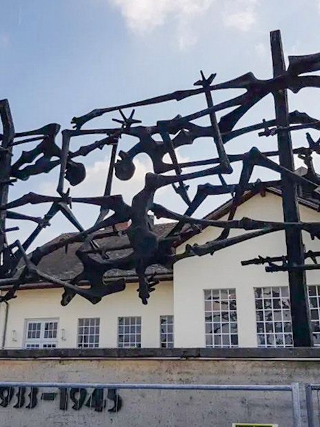 Sculpture at Dachau Concentration Camp memorializing victims, with camp building in background.