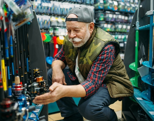 Man examining fishing reels in a tackle shop.