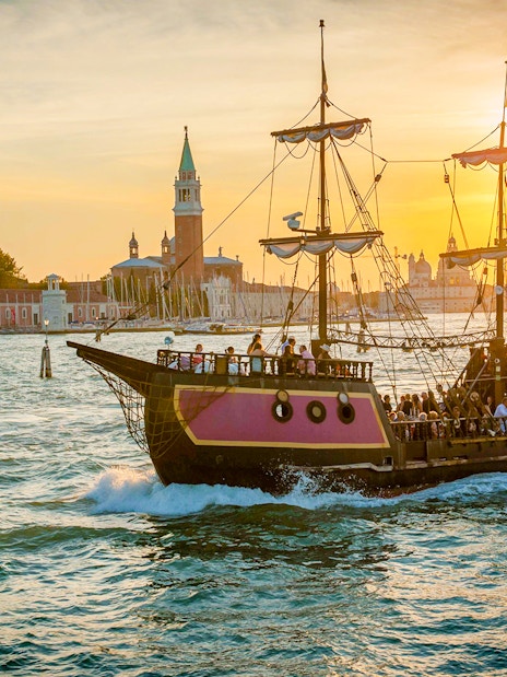 Galleon sailing at sunset near Venice landmarks during dinner cruise.