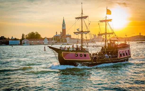Galleon sailing at sunset near Venice landmarks during dinner cruise.
