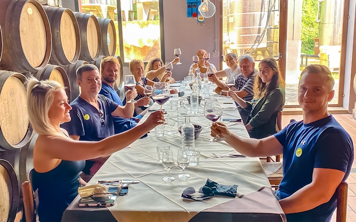 Group toasting with wine at a winery table surrounded by barrels.