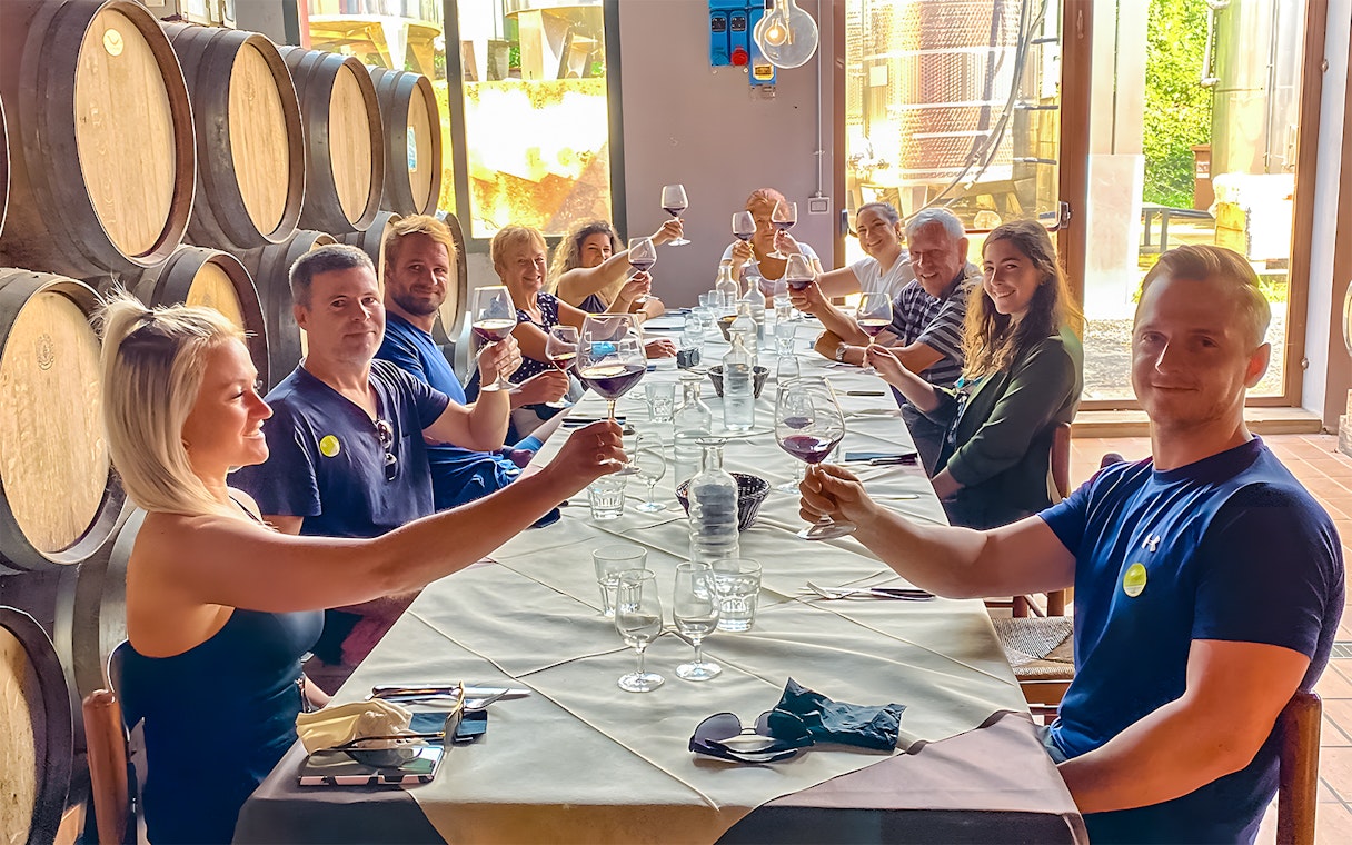Group toasting with wine at a winery table surrounded by barrels.