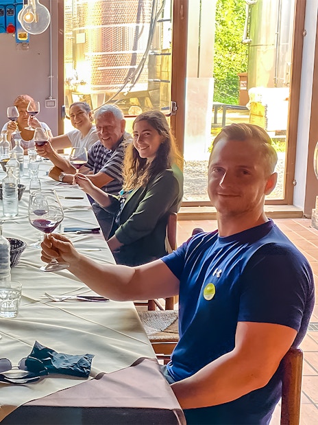 Group toasting with wine at a winery table surrounded by barrels.