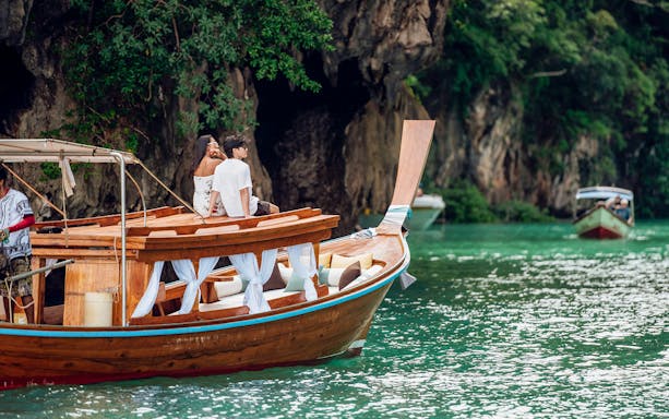 Longtail boat sailing near limestone cliffs in Krabi, Thailand.