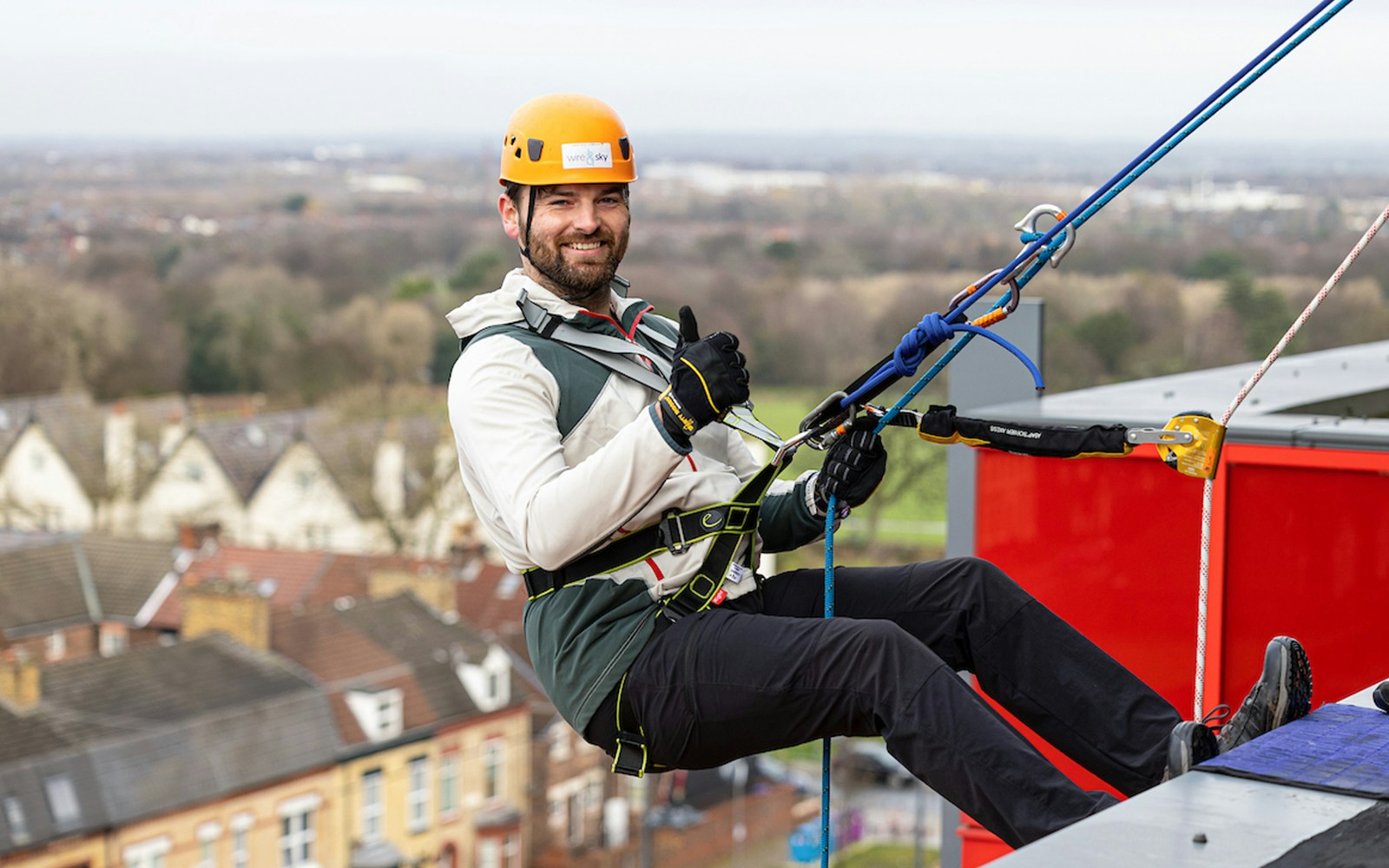 Man abseiling at Anfield Stadium, Liverpool, with city view in background.