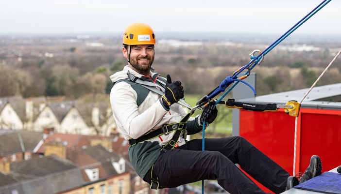 Man abseiling at Anfield Stadium, Liverpool, with city view in background.