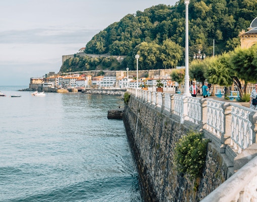 Promenade von San Sebastian mit Blick auf Küstengebäude und üppig bewachsene Hügel.