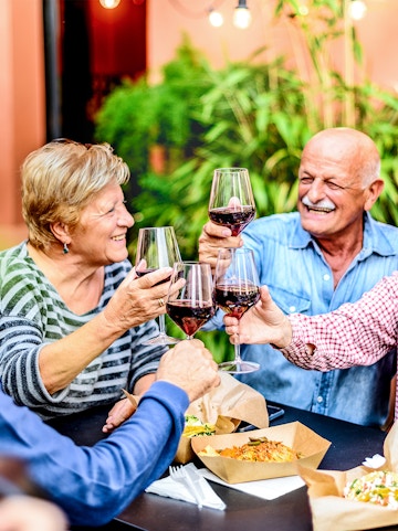 Friends enjoying wine tasting outdoors with food on the table.