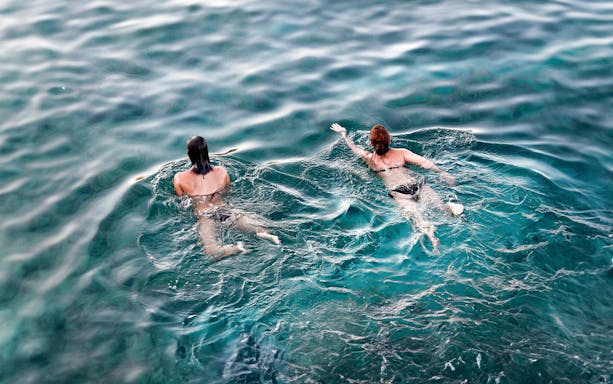 Two people swimming in clear blue water during a Syracuse boat tour.