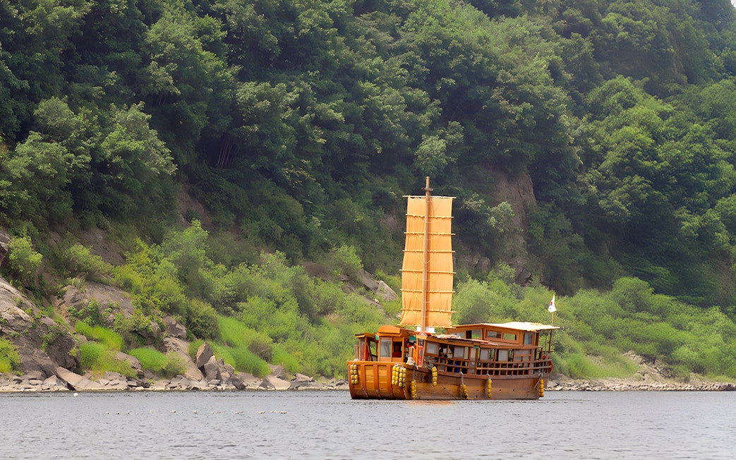 Traditional boat sailing near lush green hills on the DMZ Boat Time Leap Full Day Tour.