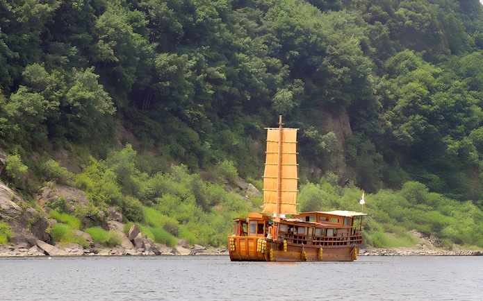 Traditional boat sailing near lush green hills on the DMZ Boat Time Leap Full Day Tour.